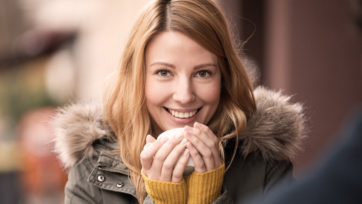 Jeune femme qui porte une veste se réchauffe avec une tasse – garantie accidents de la vie et protection cambriolage durant les mois d’automne et d’hiver