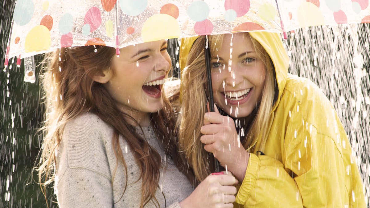 Twee jonge vrouwen lachen onder een paraplu