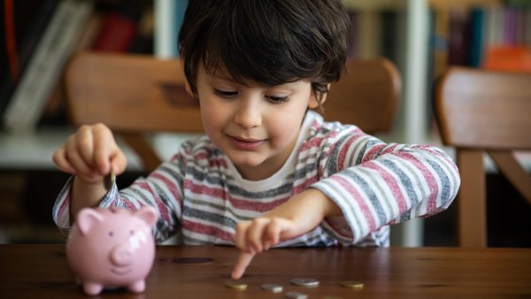 Kind met spaarvarken en munten – maandelijkse vaste kosten van het gezin 